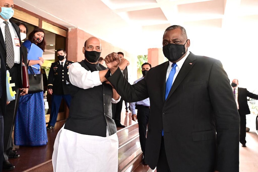 Secretary of Defense Lloyd J. Austin III and his Indian hold their forearms up together outside a building.