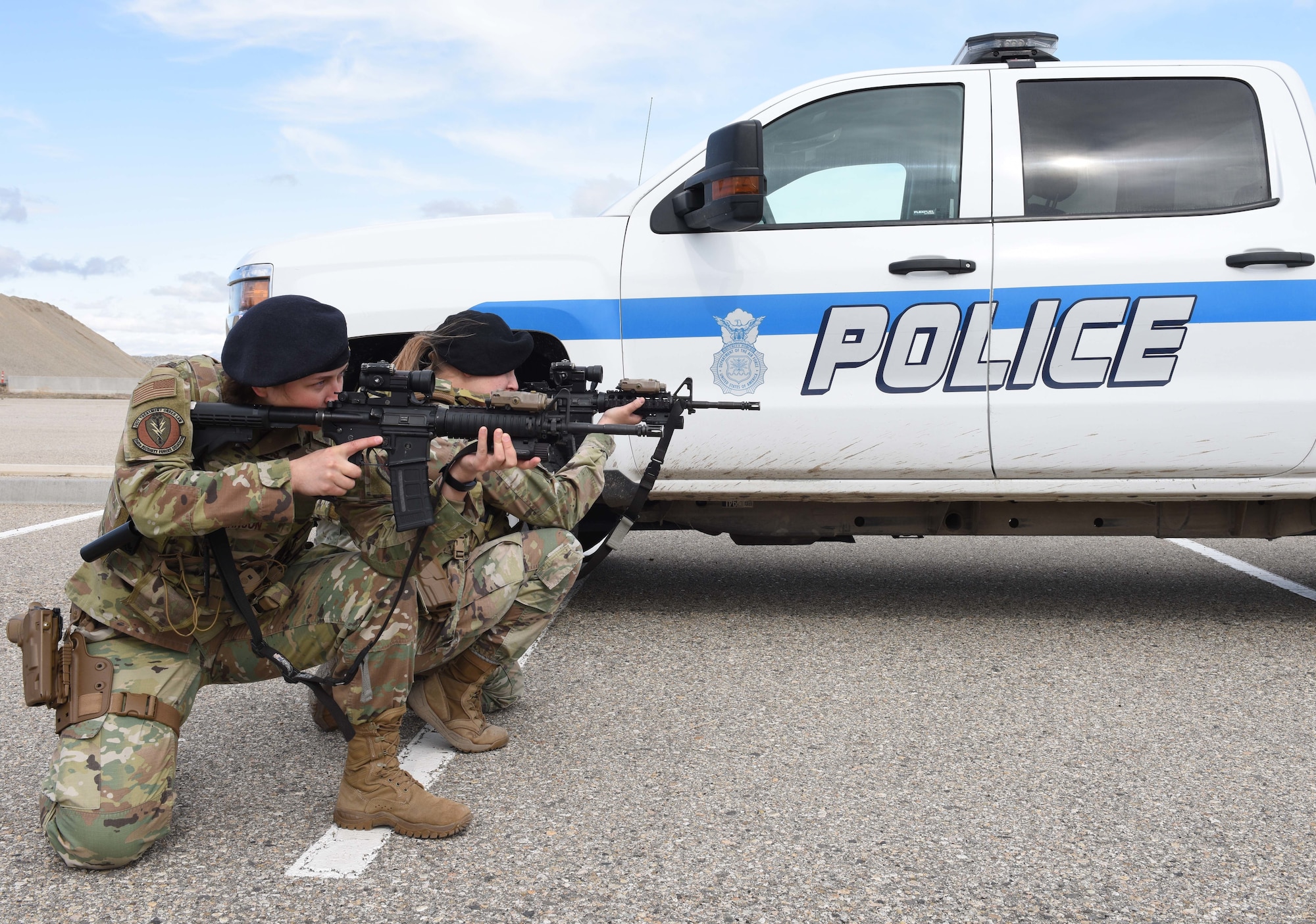 Two female Security Forces Airmen pose with their weapons in front of a police truck.