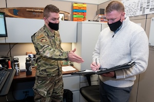 Two men standing in an office speaking to each other.