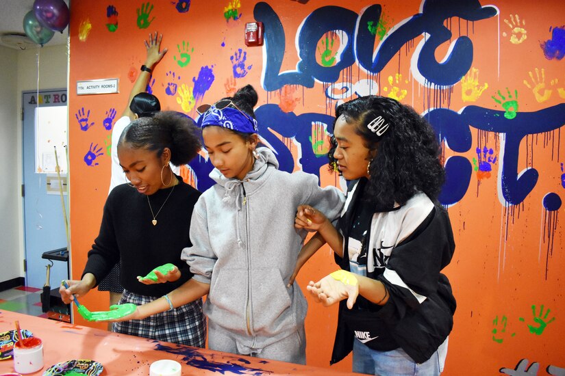 Three young girls paint their hands.