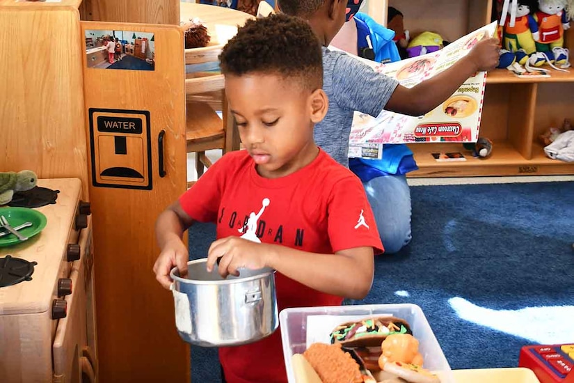 A child plays with a toy pot as others stand behind.