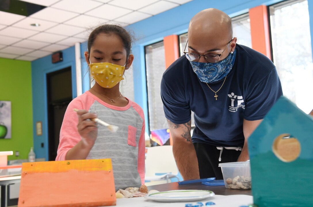 A child paints a birdhouse as man watches.