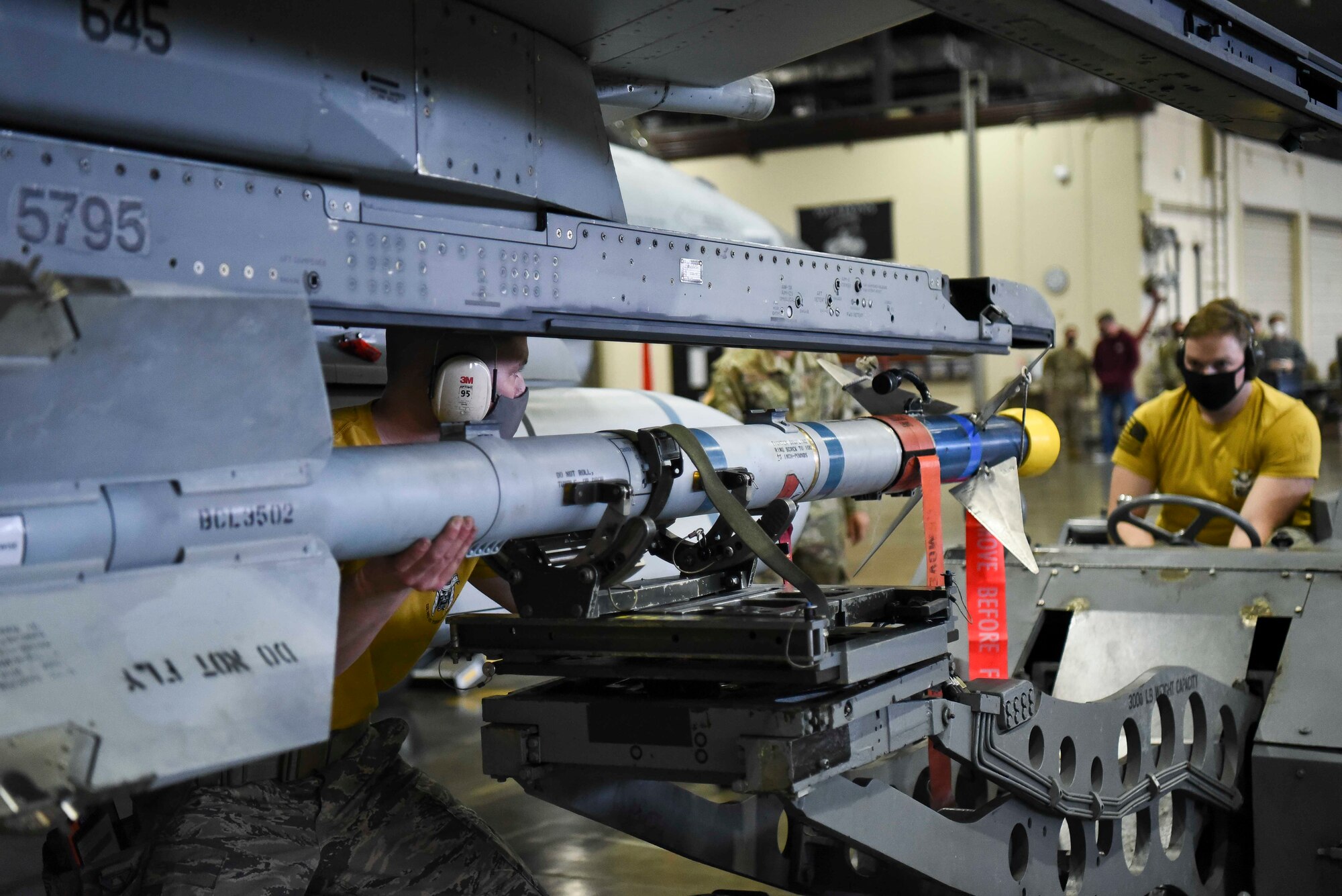 U.S. Air Force Staff Sgt. Kevin Myers, a 14th Aircraft Maintenance Unit weapons load team chief, aligns an AIM 9L/M to be attached onto an F-16 Fighting Falcon while Airman 1st Class Austin Winkelspecht, a 14th Aircraft Maintenance Unit weapons load crew member, drives the MJ-1 bomb lift truck to transport the missile during the fourth quarter load competition at Misawa Air Base, Japan, March 19, 2021.