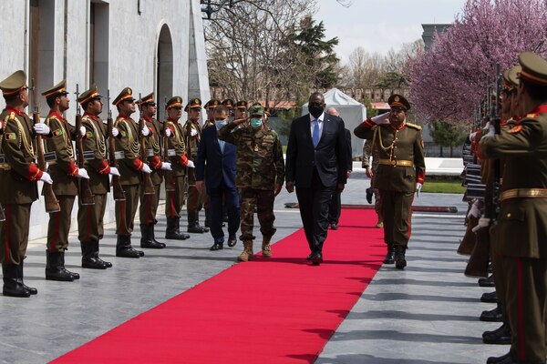 Defense Secretary Lloyd J. Austin III walks along a red carpet with military officials.
