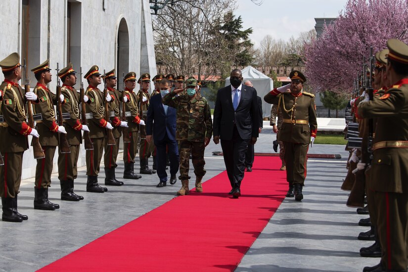 Defense Secretary Lloyd J. Austin III walks along a red carpet with military officials.