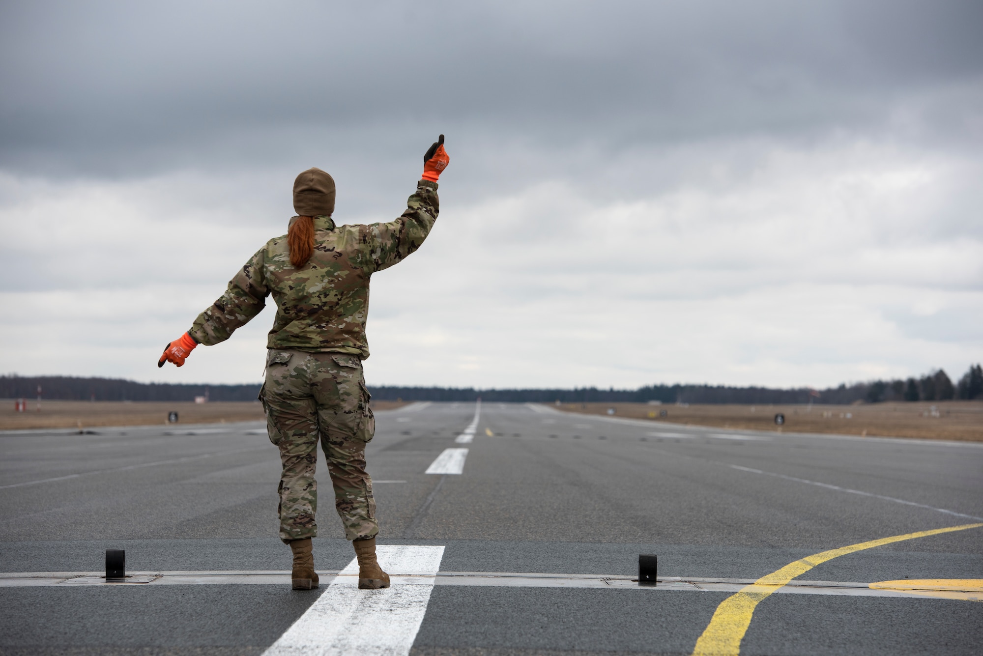 U.S. Air Force Airman 1st Class Chelsea Glasscock, 435th Construction and Training Squadron Aircraft Arresting System Depot apprentice, gives the signal to reel in the cable system during a Barrier Arresting Kit certification at Ämari Air Base, Estonia, March 17, 2021. The BAK is certified annually to test the stability and effectiveness of the system, which acts as a braking mechanism to stop the aircraft in the event of an emergency that would prevent the aircraft from performing a standard landing. (U.S. Air Force photo by Airman 1st Class Jessi Monte)