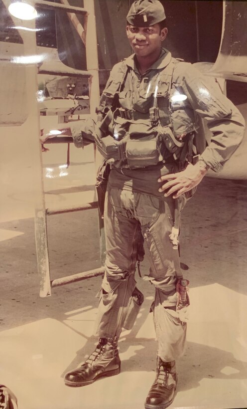 A young man wearing a military uniform rests his hand on a ladder.