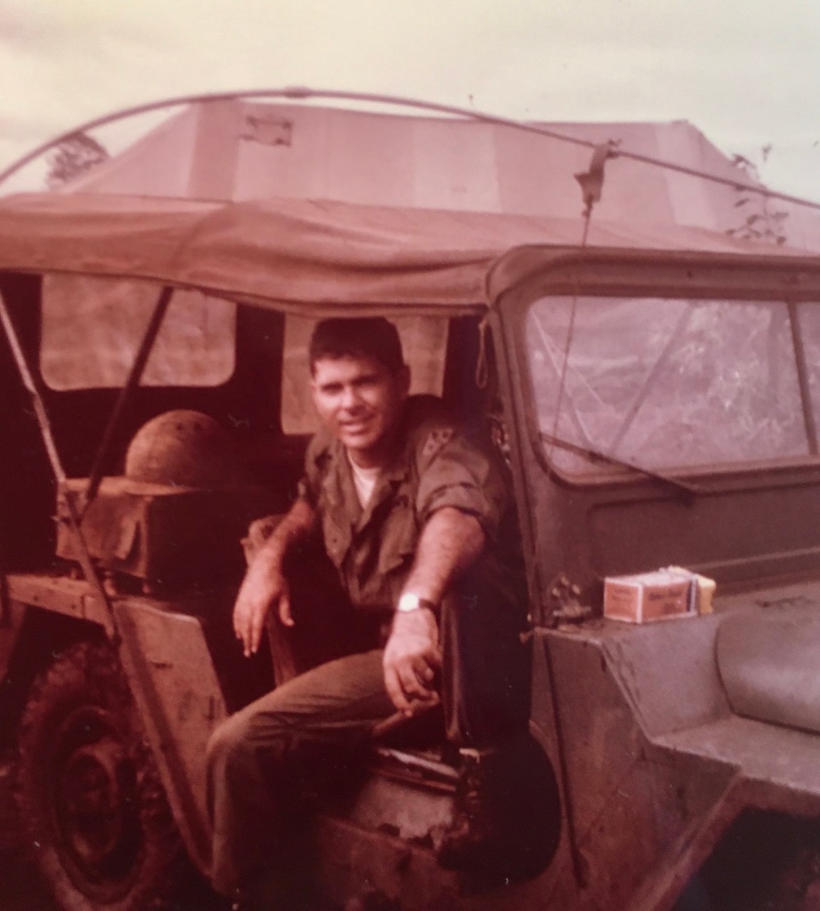 A young man in Vietnam-era Army fatigues looks out from a jeep.