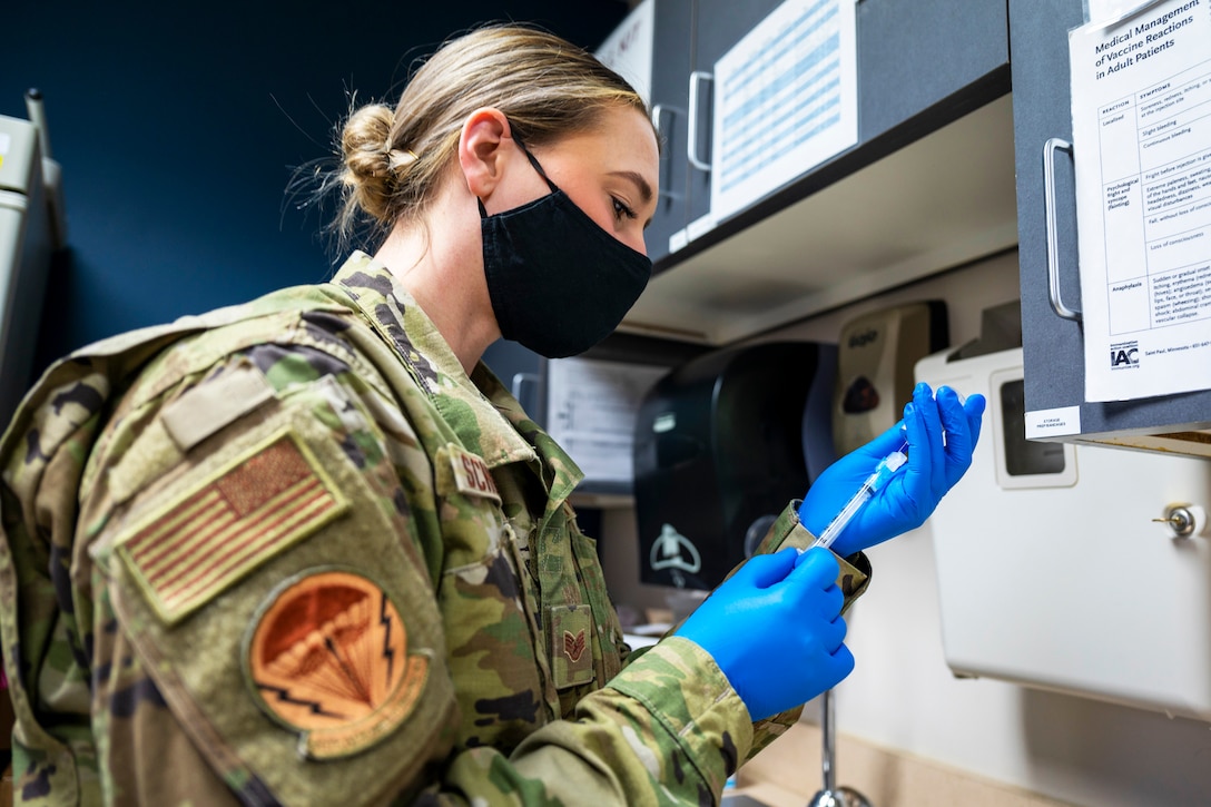 An airman wearing a face mask and gloves holds a syringe while preparing a vaccine.