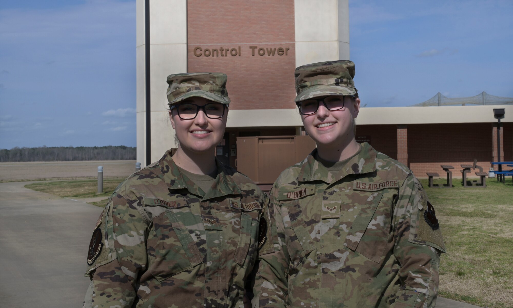 U.S. Air Force Senior Airman Laura O’Brien and Airman 1st Class Allison O’Brien, 14th Flying Training Wing air traffic controllers, stand together in front on the control tower, Mar. 11, 2021, on Columbus Air Force Base, Miss. The Airmen are sisters who share the same Air Force Specialty Code and are stationed at the same base. (U.S. Air Force photo by Airman 1st Class Jessica Haynie)