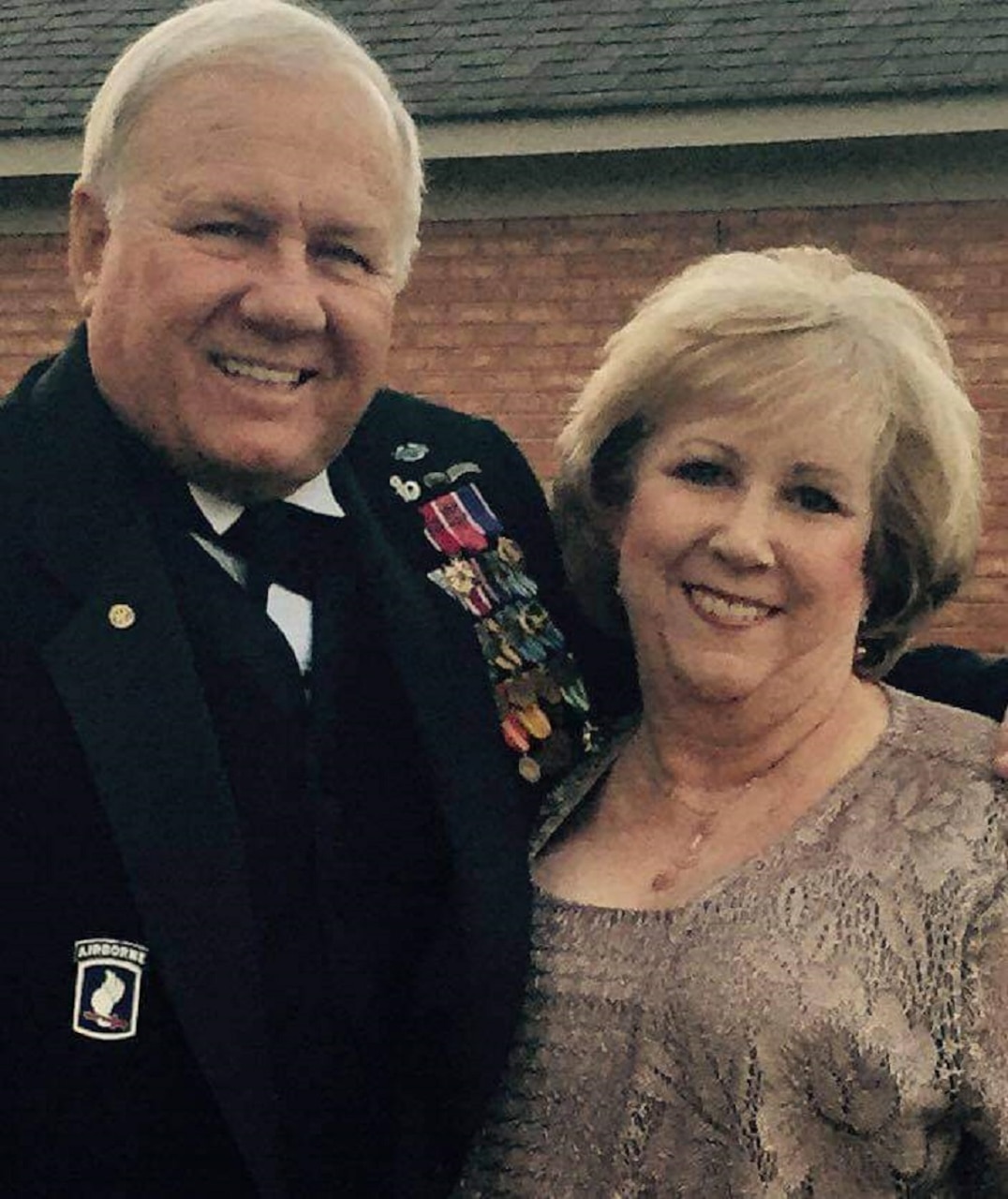 A man in an Army dress uniform hugs a woman.