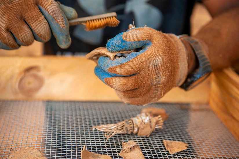 An airmen uses a brush to clean dusty debris.