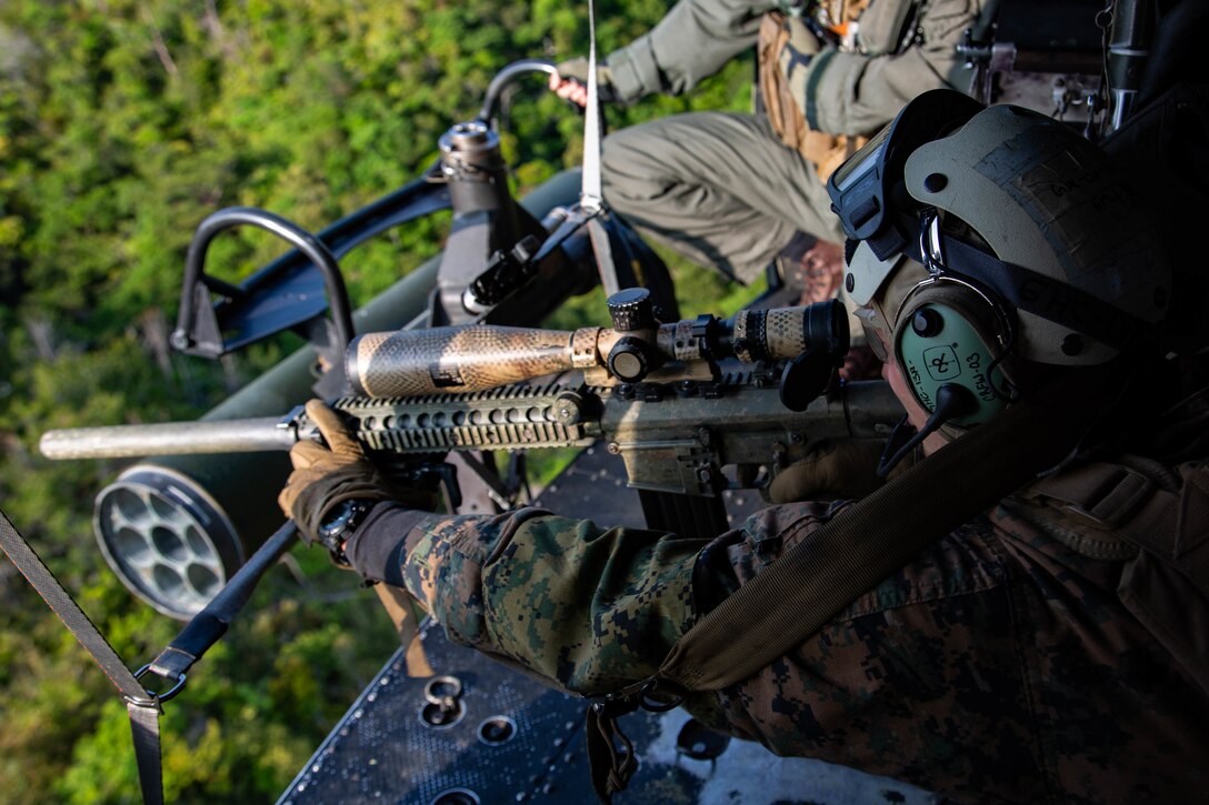 A machine gunner takes aim out of a helicopter.