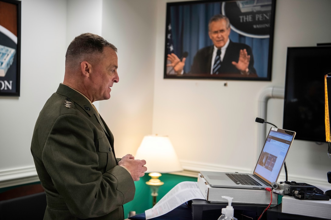 A man in a military uniform stands in front of a laptop computer.