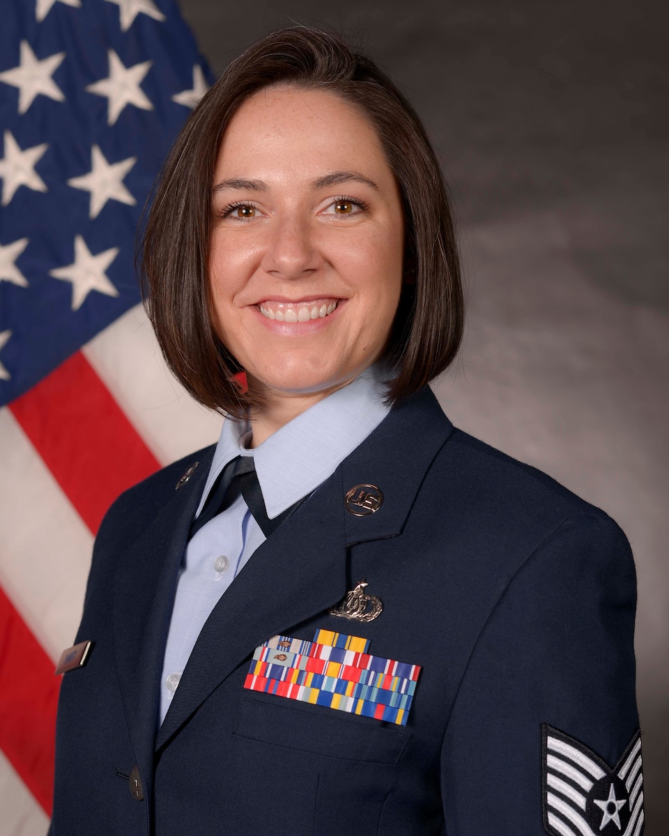 An Airman in uniform poses in front of a flag