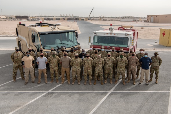 Firefighters pose in front of two firetrucks