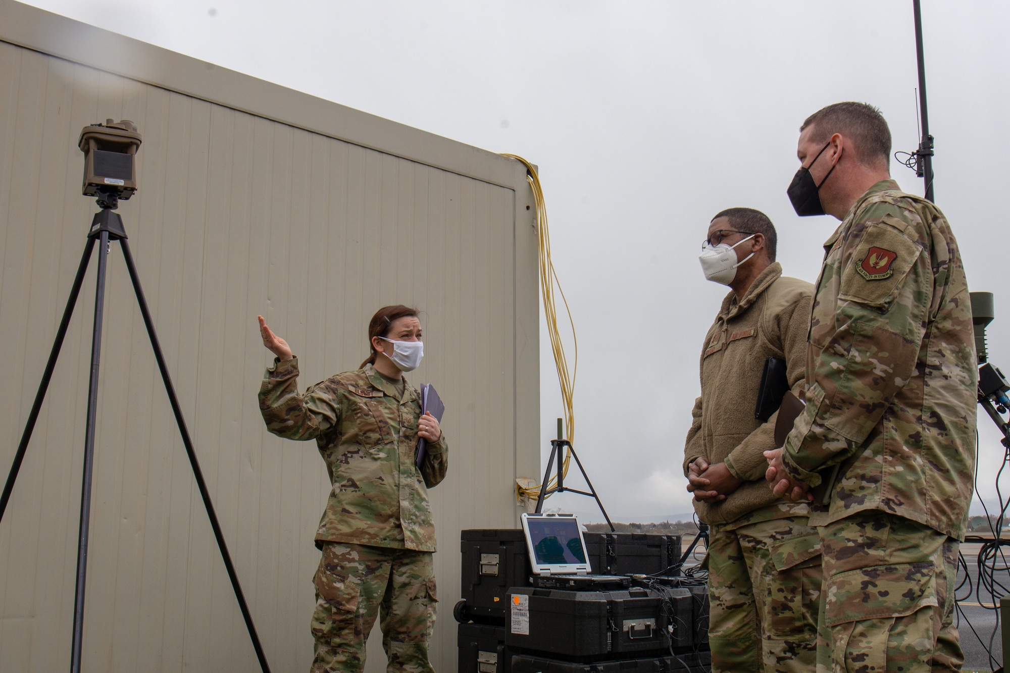 Three people outside look at weather equipment.