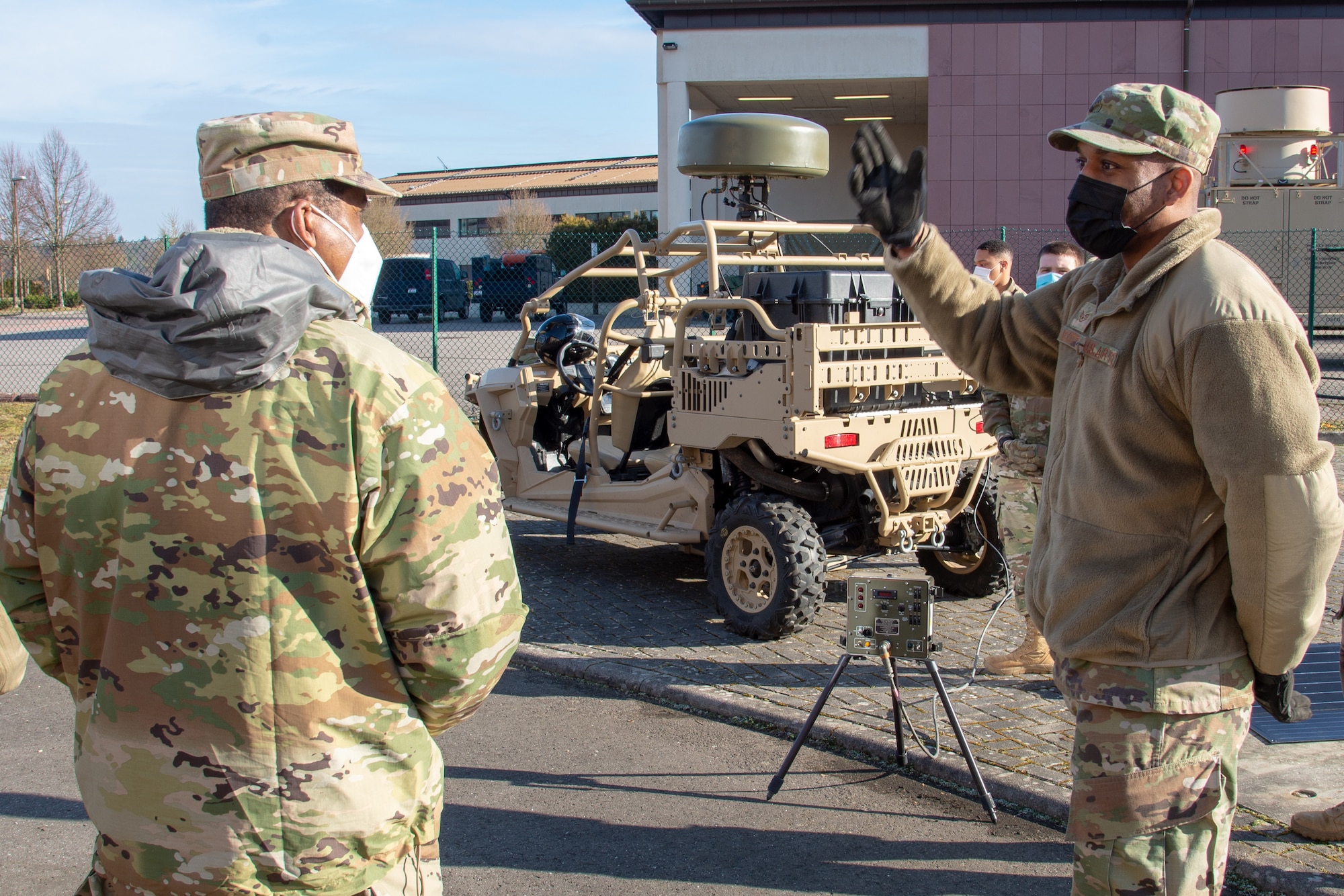 Two man stand speaking to each other with equipment in the background.