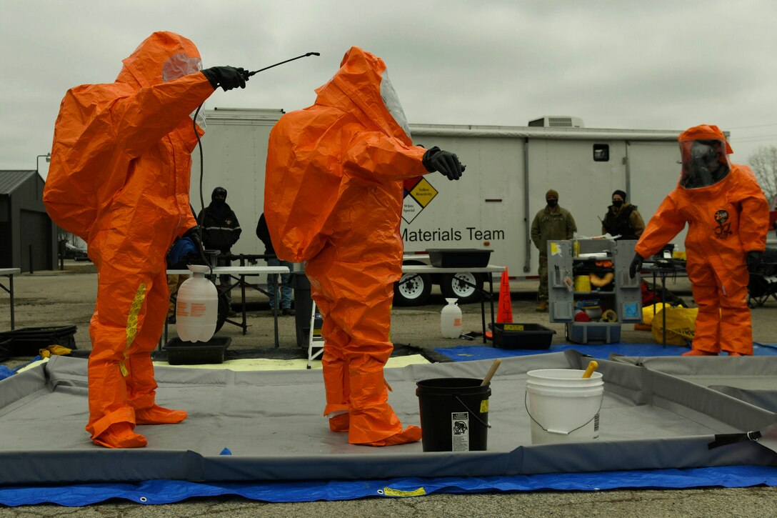 Guardsmen wearing hazmat suits perform decontamination procedures.