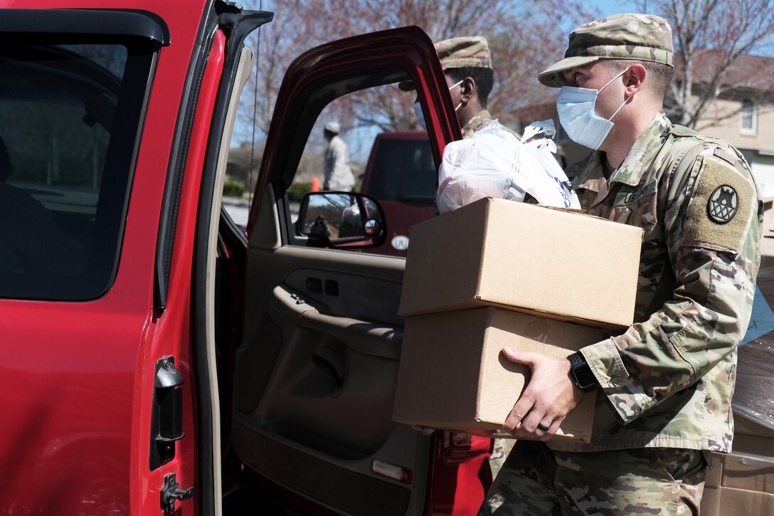 Two soldiers wearing face masks put boxes of food into a vehicle for residents during a food distribution event.