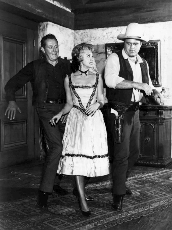 A woman and two men, dressed in 19th century costumes, appear on the set of a western TV series.