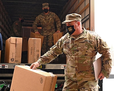 Soldiers in uniforms unload boxes from a truck with computers in them.