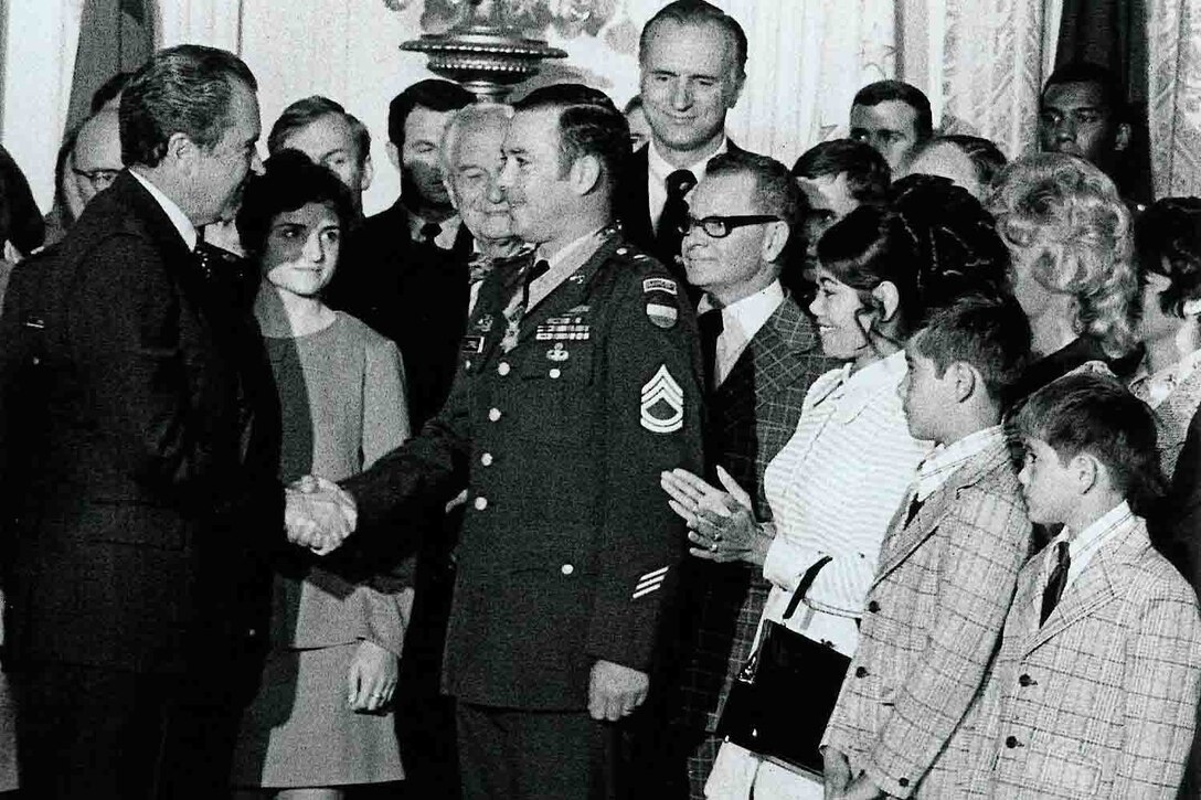 A soldier shakes hands with a man as people around him clap.