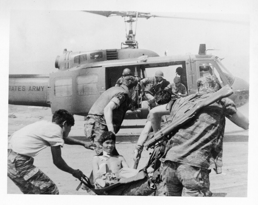 Soldiers carry a shirtless man on a stretcher to a helicopter.