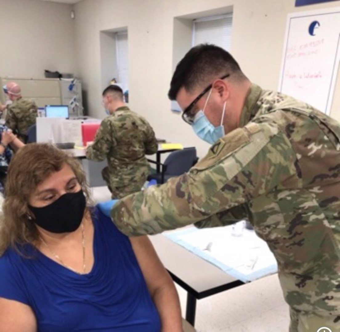 Staff Sgt. David Bravo, a combat medic with the Massachusetts National Guard, vaccinates his mother at East Boston Neighborhood Health Center. Bravo and other Massachusetts National Guard members were activated to distribute Pfizer COVID vaccines in Massachusetts.