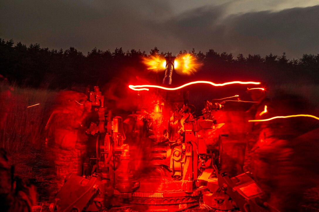 Marines fire a weapon in a field illuminated by red lights.