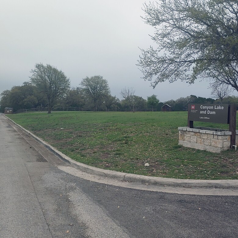 Canyon Lake Office sign in grass yard with trees next to a road