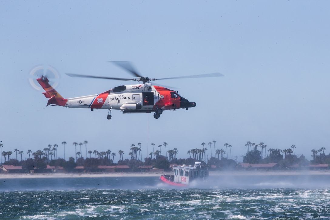 A Coast Guard helicopter hovers above a Coast Guard boat in choppy water.