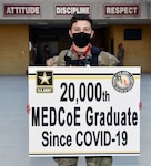 Sgt. Carter McCall holds a sign that signifies him as the 20,000th U.S. Army Medical Center of Excellence graduate since COVID-19.