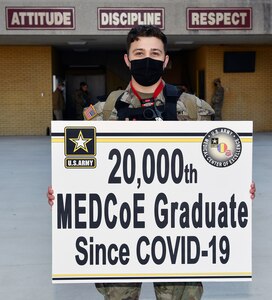 Sgt. Carter McCall holds a sign that signifies him as the 20,000th U.S. Army Medical Center of Excellence graduate since COVID-19.