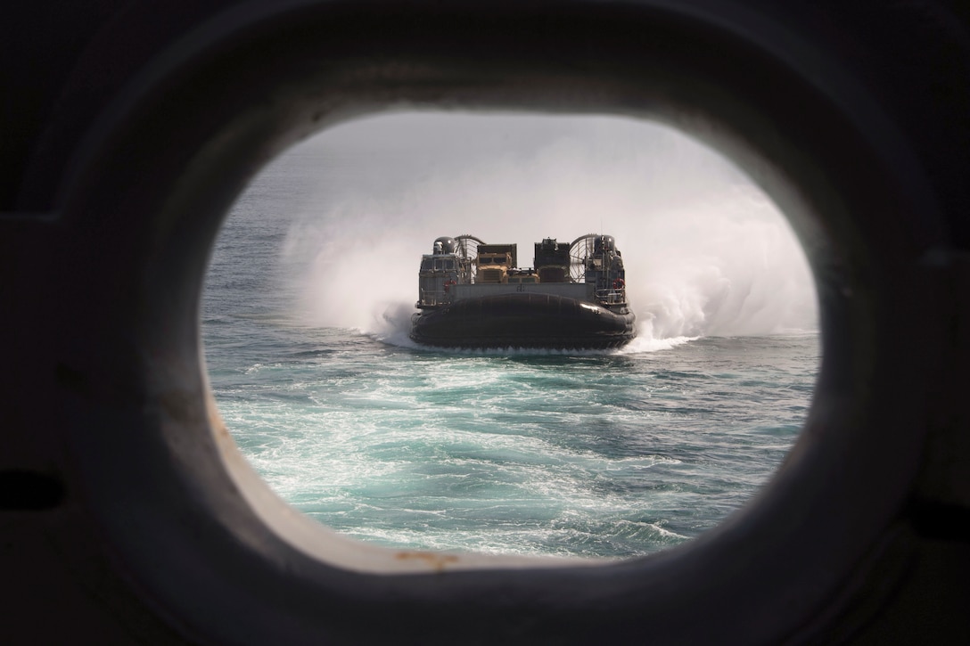 A small boat approaches a ship as seen through a porthole.
