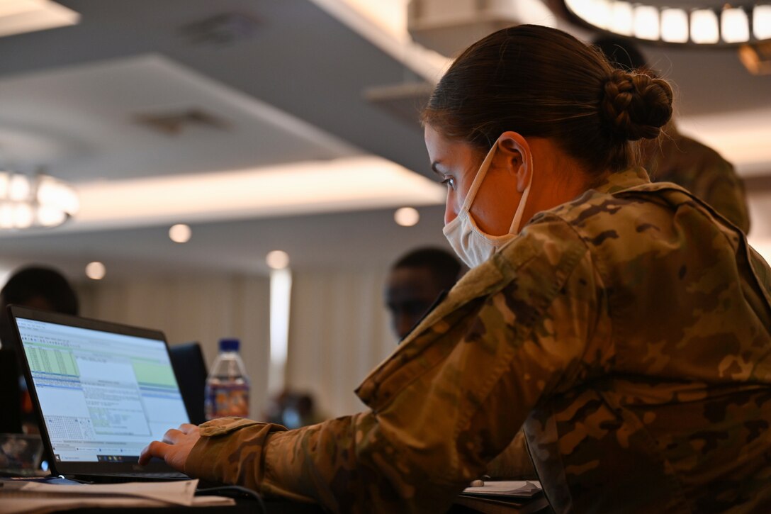 A woman in a military uniform types on a laptop.