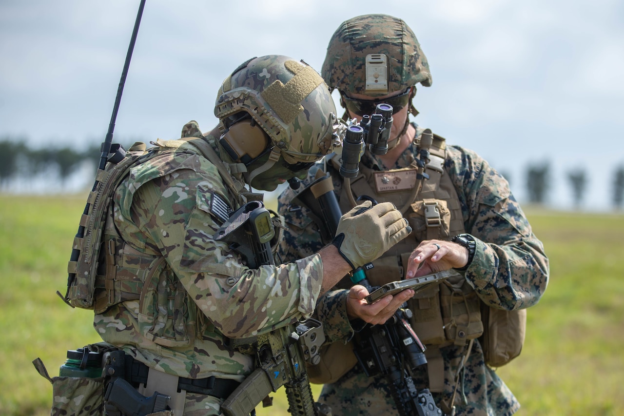 Two troops look at a screen in the middle of a field.