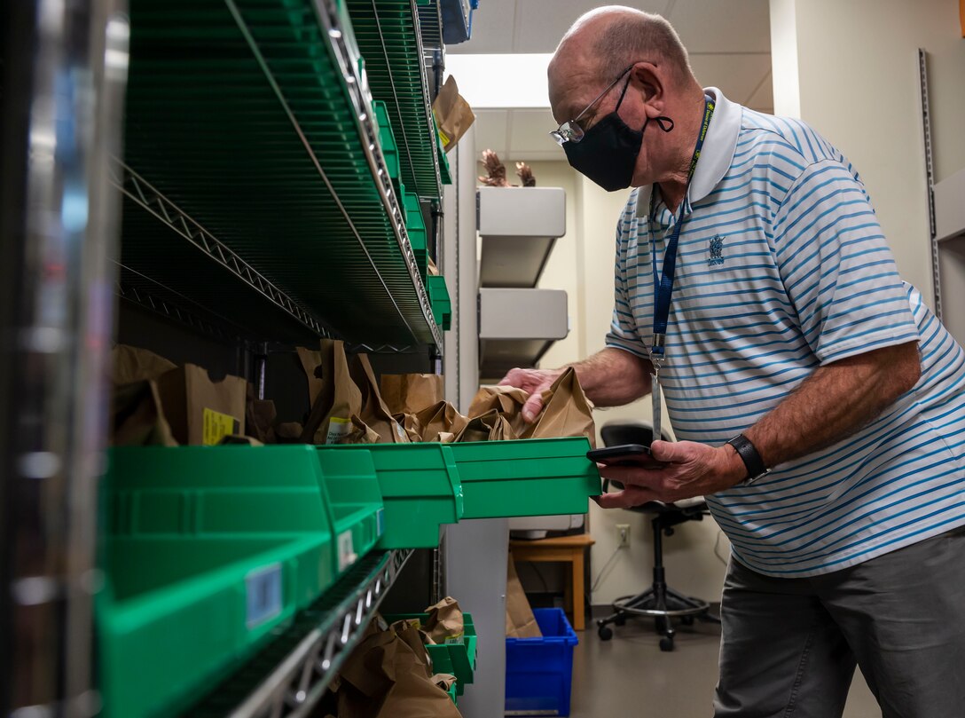 Eugene Johnson, pharmacy volunteer, searches for a prescription at the 436th Medical Group pharmacy on Dover Air Force Base, Delaware, March 12, 2021. Prescriptions are stored in organized bins until they are ready to be delivered to patients. (This photo has been digitally enhanced to protect patient information) (U.S. Air Force photo by Airman 1st Class Cydney Lee)
