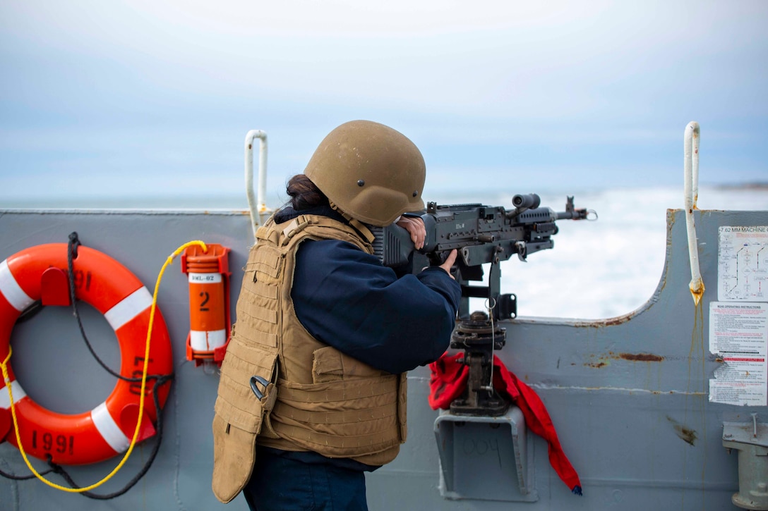 A sailor looks through the scope of a weapon on the deck of a vessel.