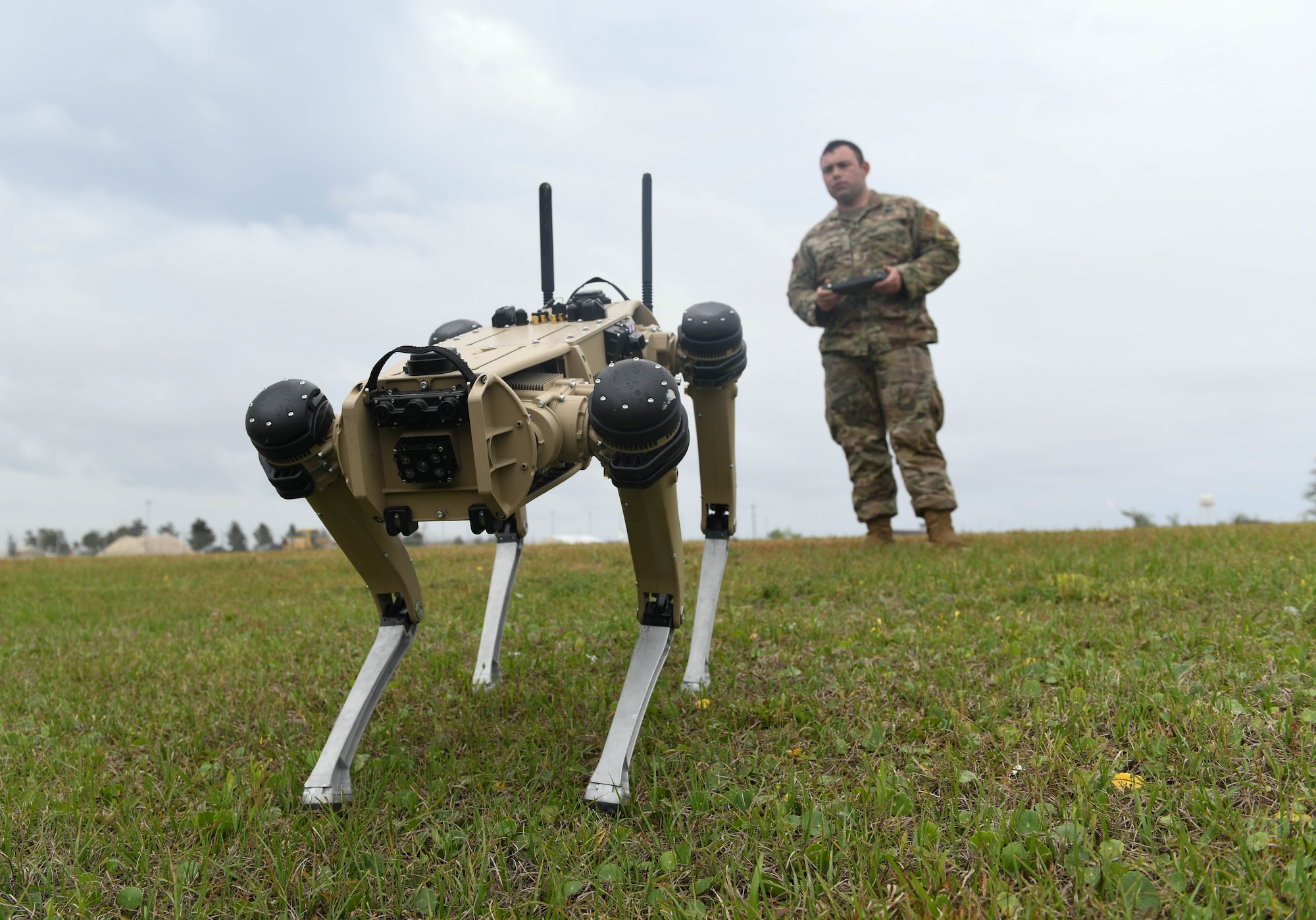 A uniformed Airman is controlling a robot dog by it's controller