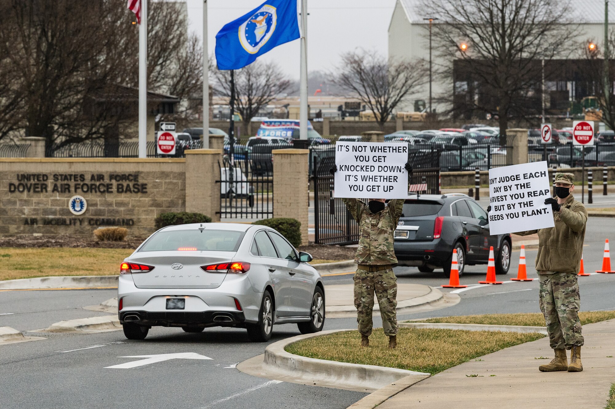 Staff Sgt. Jason Bravard, center, and Tech. Sgt. Jared Rykse, right, both 436th Airlift Wing religious affairs Airmen, hold signs displaying positive affirmations as vehicles approach the main gate on Dover Air Force Base, Delaware, March 24, 2021. Bravard, Rykse and other members of Team Dover held signs as personnel approached the base. (U.S. Air Force photo by Roland Balik) (This photo has been altered for security purposes by blurring out personal identifiable information.)