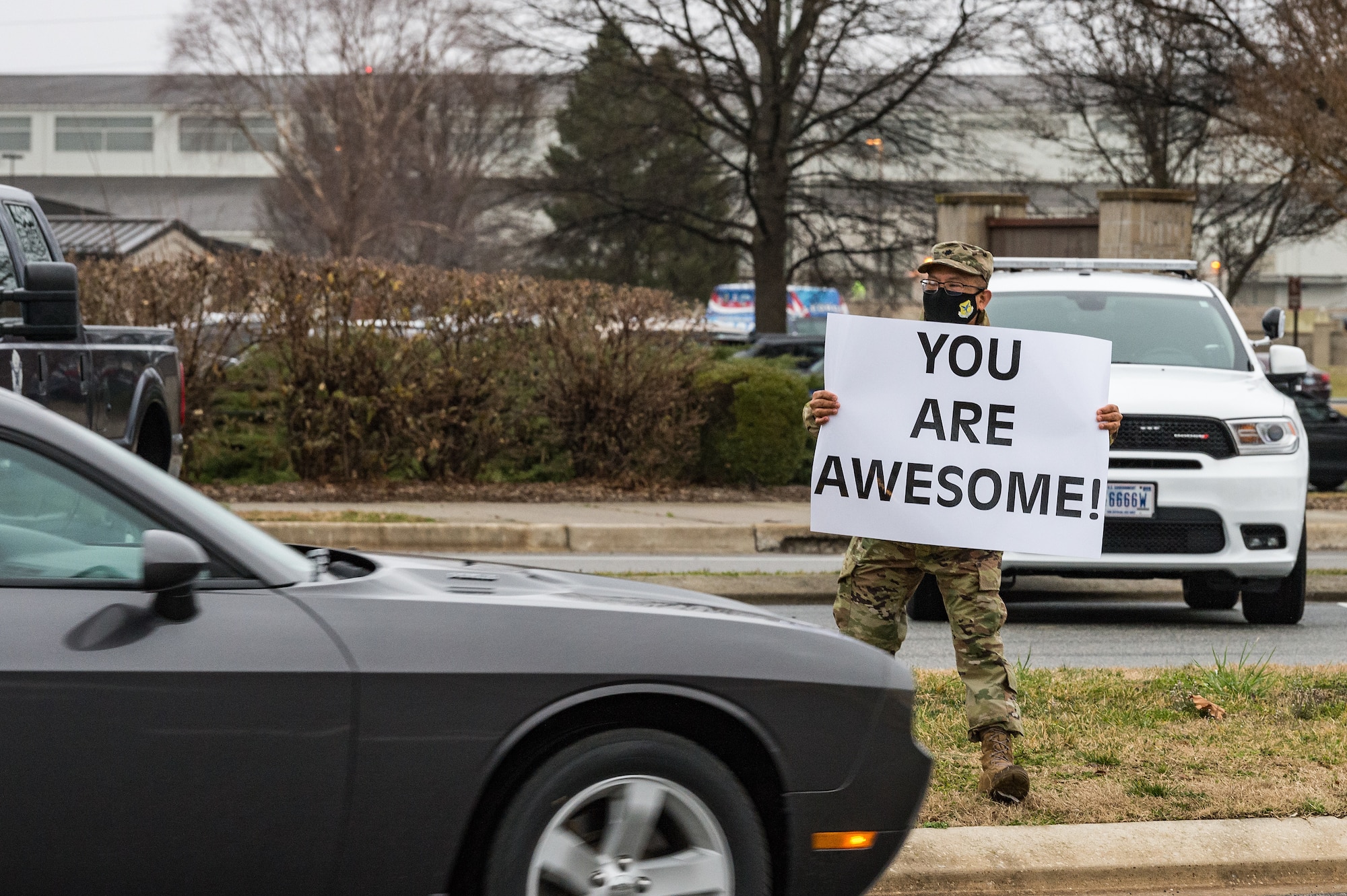 Lt. Col. Abner Valenzuela, 436th Airlift Wing head chaplain, holds a sign displaying a positive affirmation as vehicles pass through the main gate on Dover Air Force Base, Delaware, March 24, 2021. Valenzuela and other members of Team Dover held signs as vehicles approached and entered the base. (U.S. Air Force photo by Roland Balik)