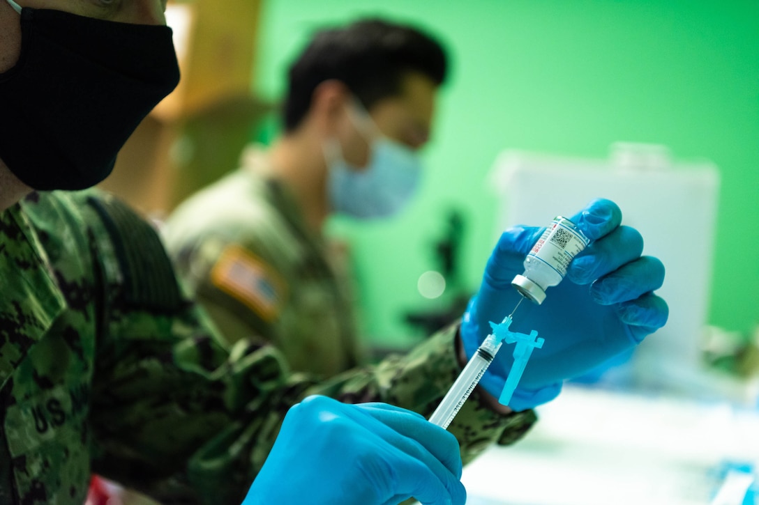 A service member puts vaccine into a syringe.