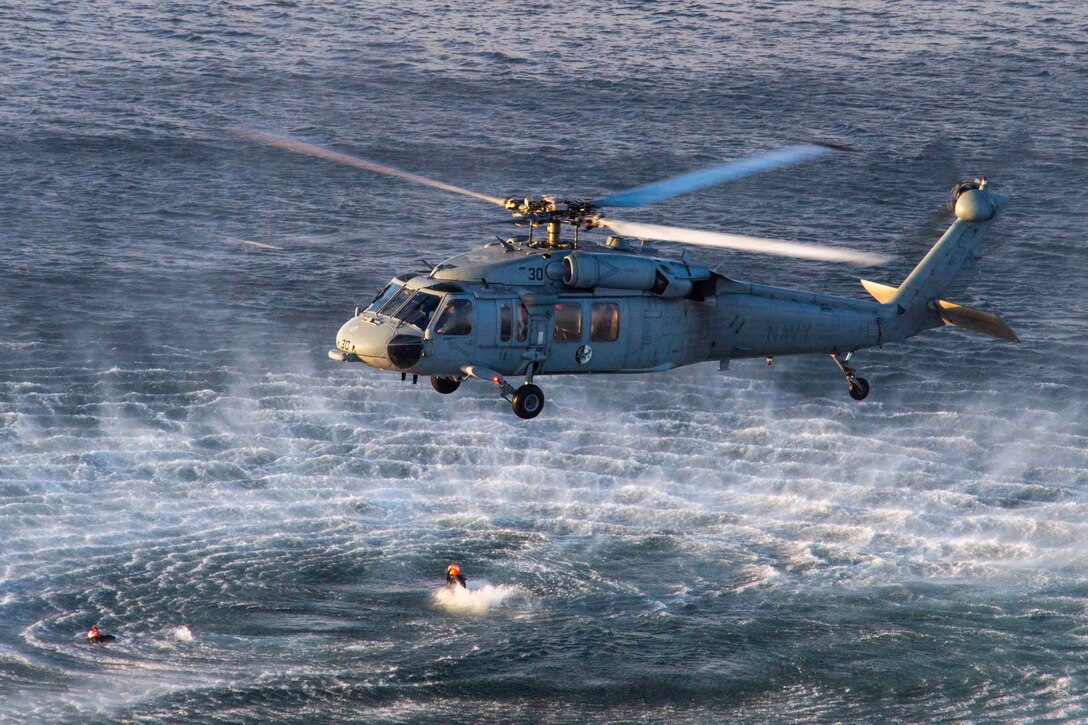 A Navy helicopter hovers over water.