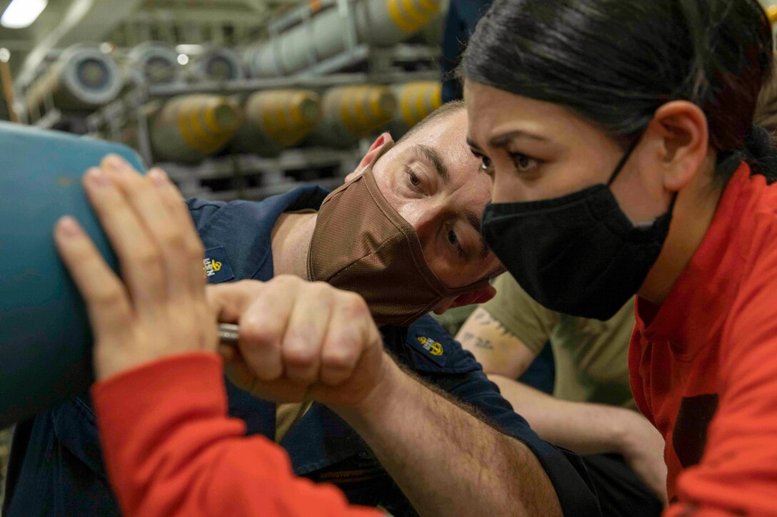 A sailor teaches a fellow sailor how to build a simulated bomb.
