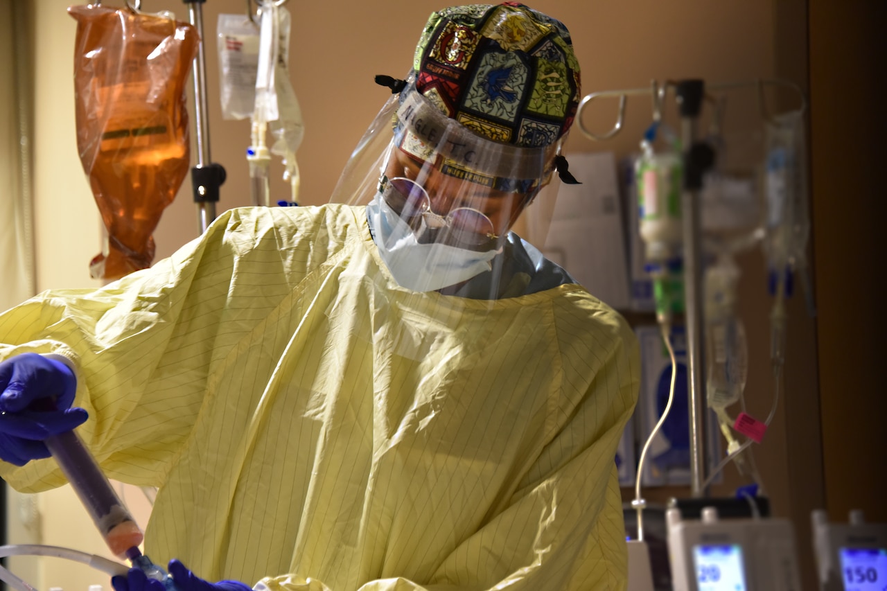 A female soldier wearing gloves, face mask and a face shield conducts a medical procedure.