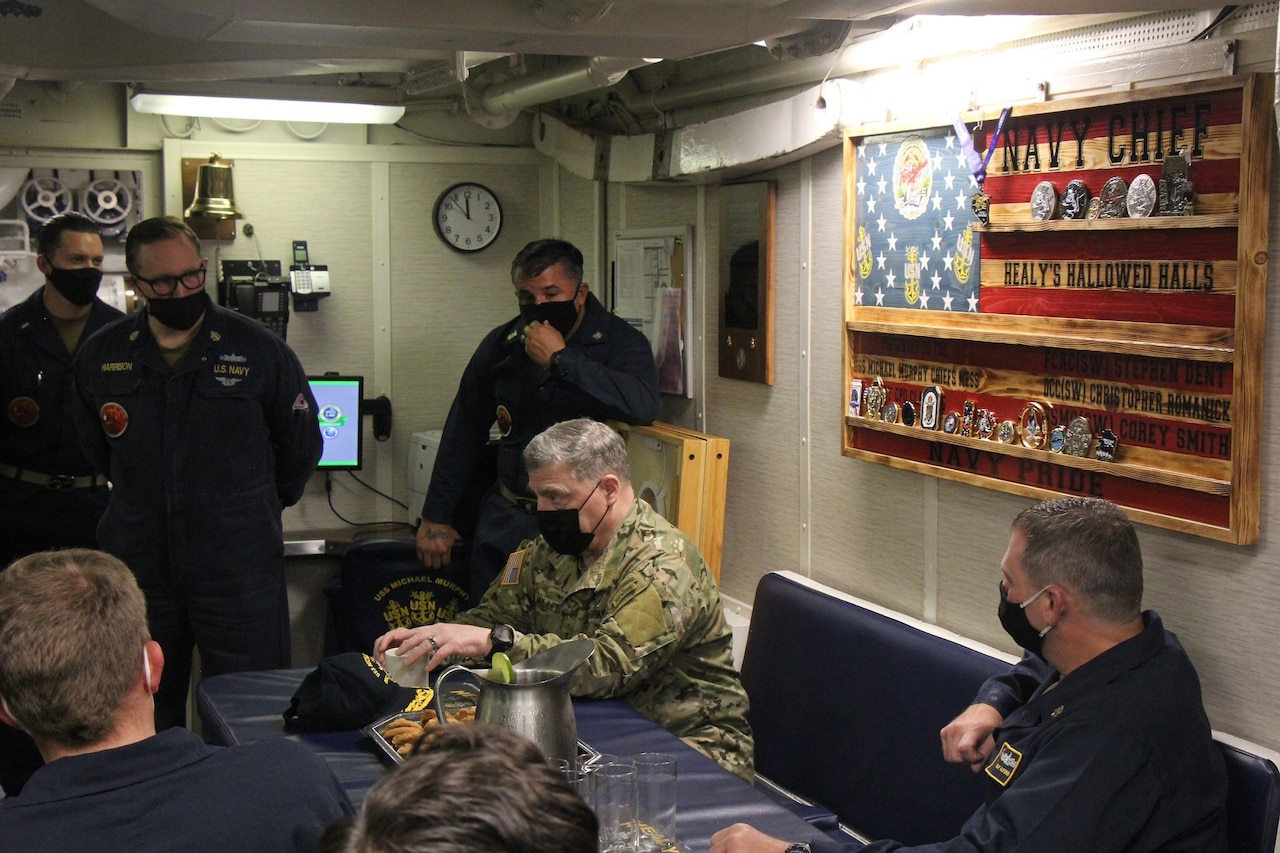 Military personnel sit at a conference table and talk.