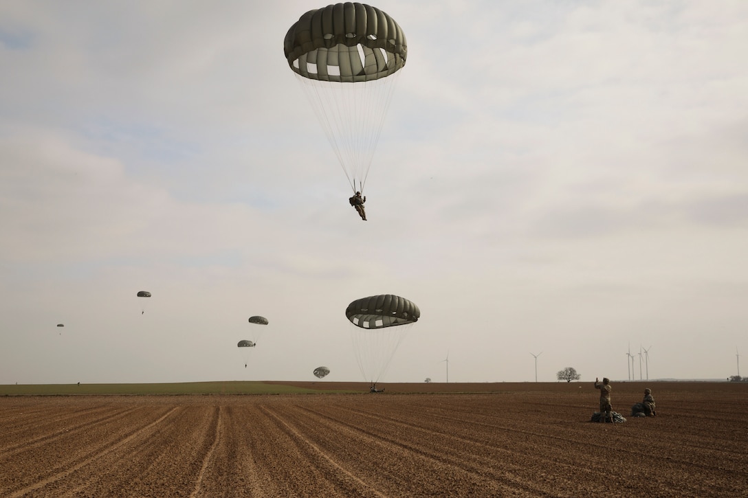 Soldiers freefall while wearing parachutes over a field.