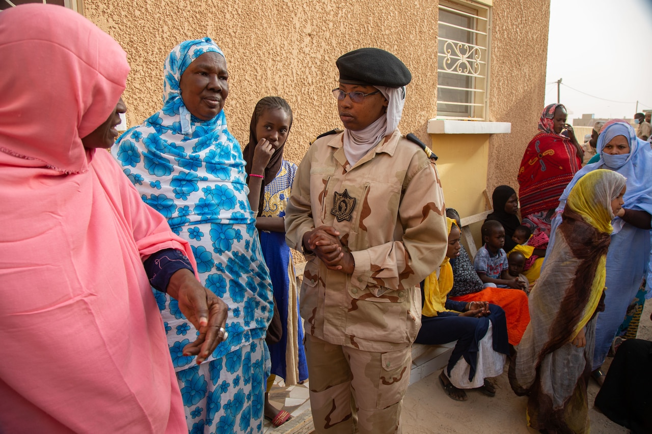 Mauritanian woman soldier speaks with women in colorful dresses outside a clinic.