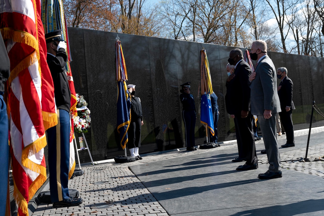 Secretary of Defense Lloyd J. Austin III, Secretary of Veterans Affairs Denis R. McDonough and others stand before a wreath placed at the Vietnam Veterans Memorial Wall.